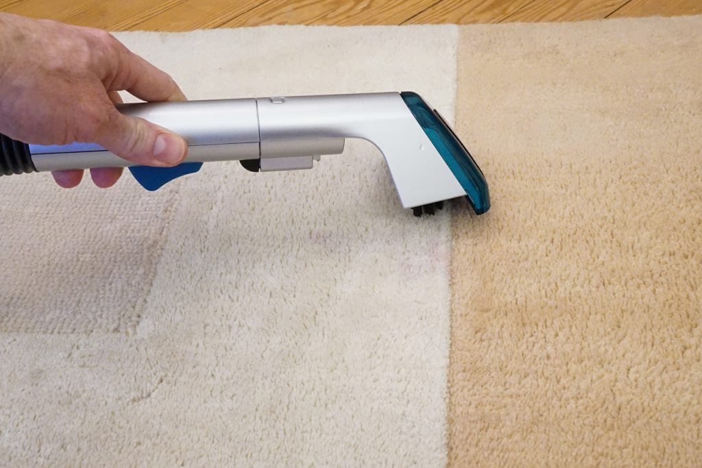 Hand using Hoover CleanJet carpet cleaner on a beige carpet.