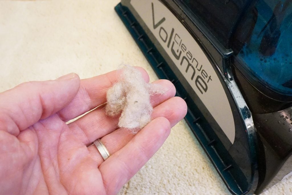 Hand holding dirt next to Hoover CleanJet carpet cleaner.