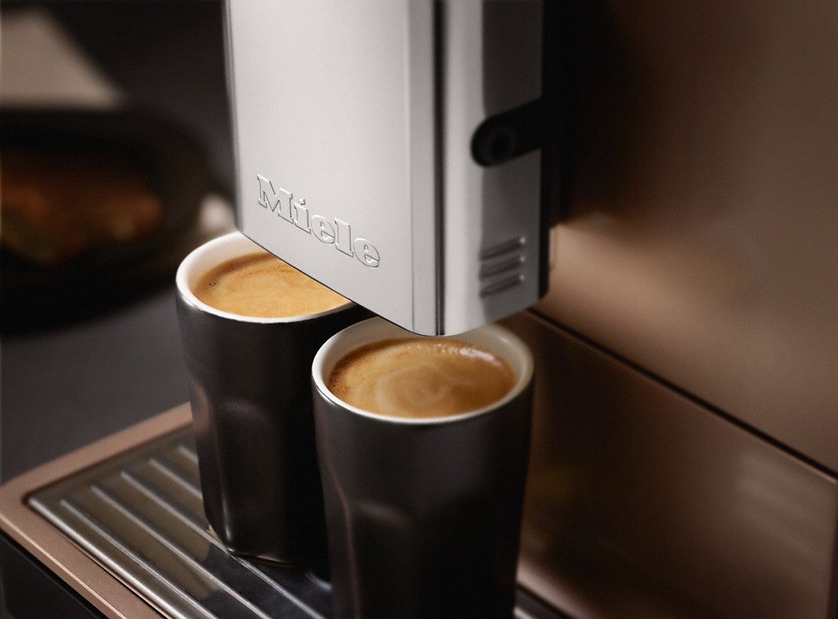 Miele CM5500 coffee machine in rose gold and black.Miele CM5500 coffee machine dispensing espresso into cups.