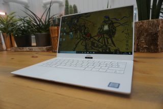 Dell XPS 13 laptop on wooden table with plant background.
