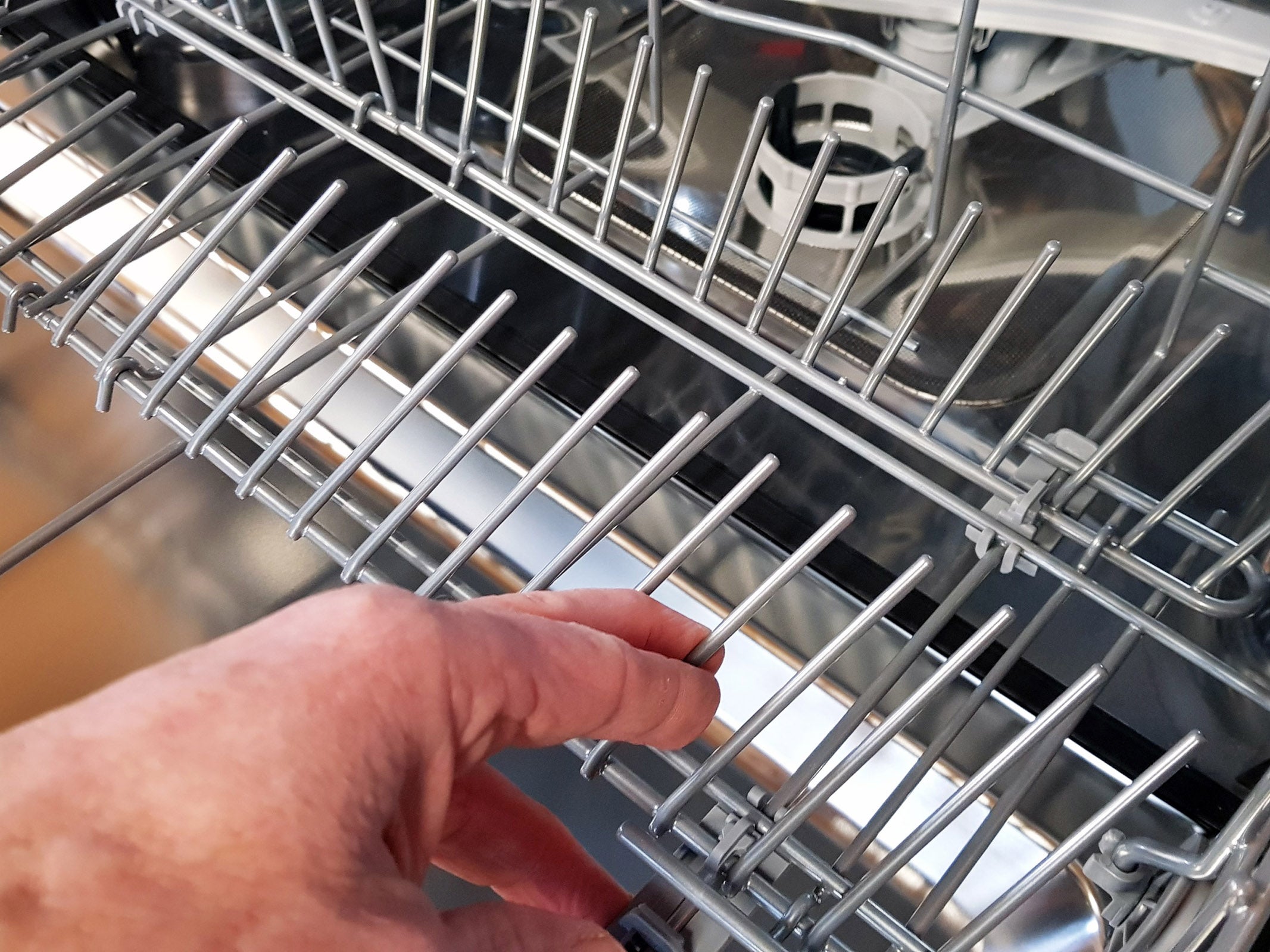 Hand examining the upper rack of an Indesit dishwasher.