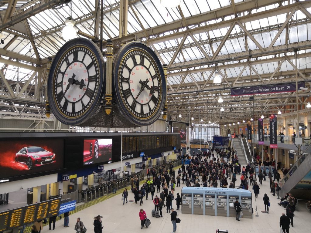 Train station interior with large clocks and busy commuters.