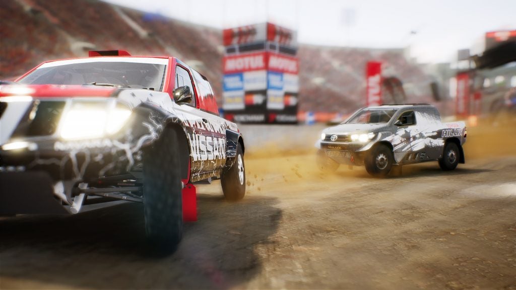Racing trucks competing on a dusty gravel track.