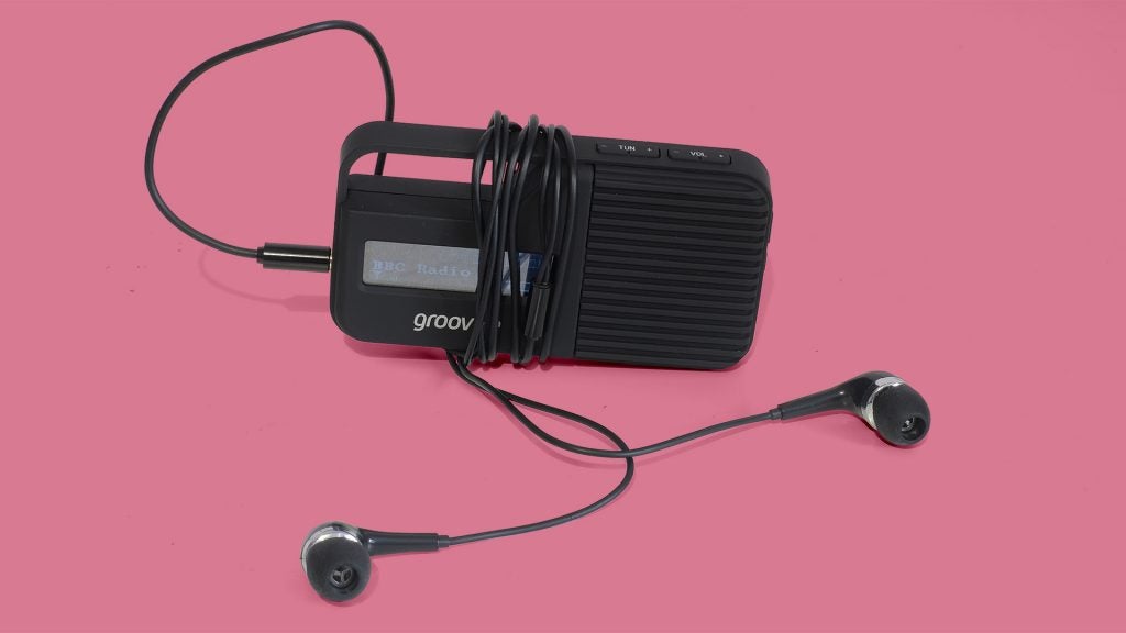 Groov-e Rio portable radio with earphones on pink background.