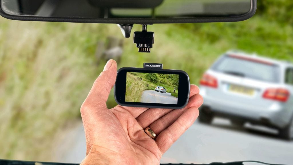 Nextbase 612GW dash cam held in hand with road view.