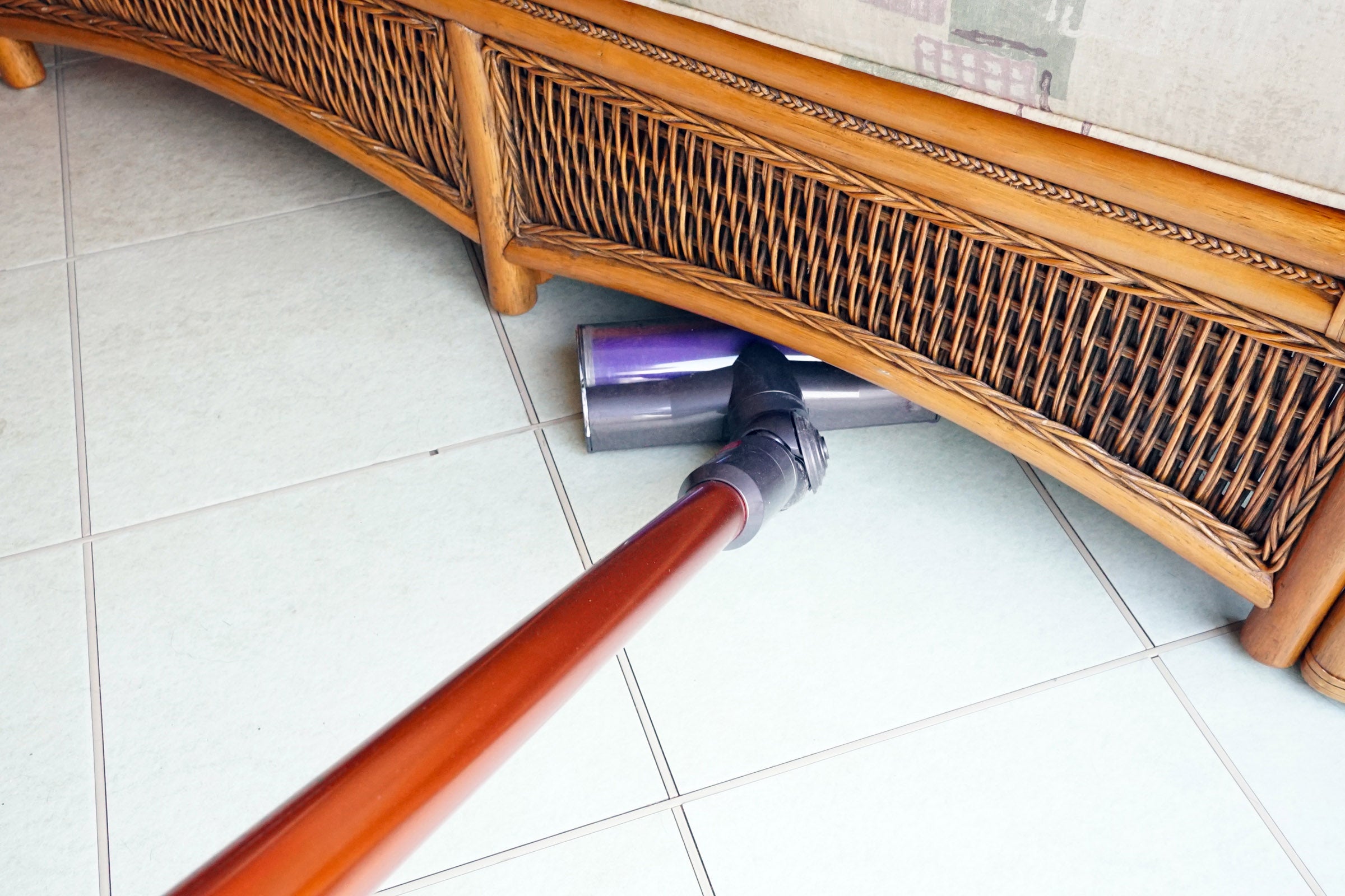 Dyson Cyclone V10 vacuum cleaning under a wicker couch.
