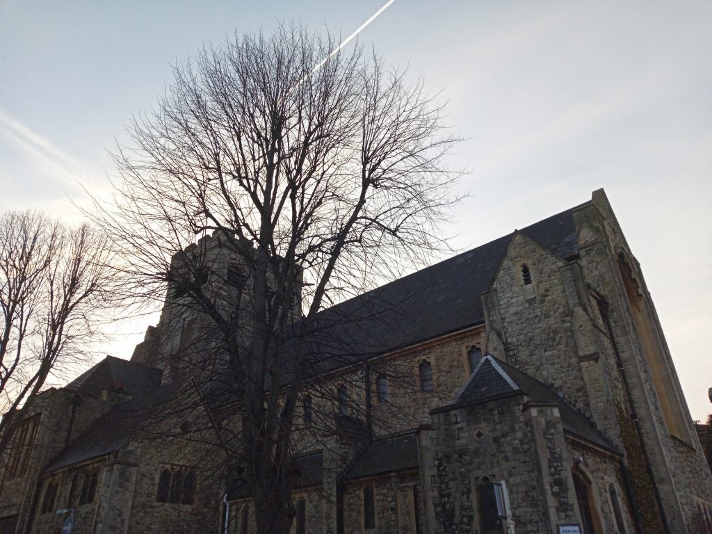 Old stone church with bare trees against a clear sky.
