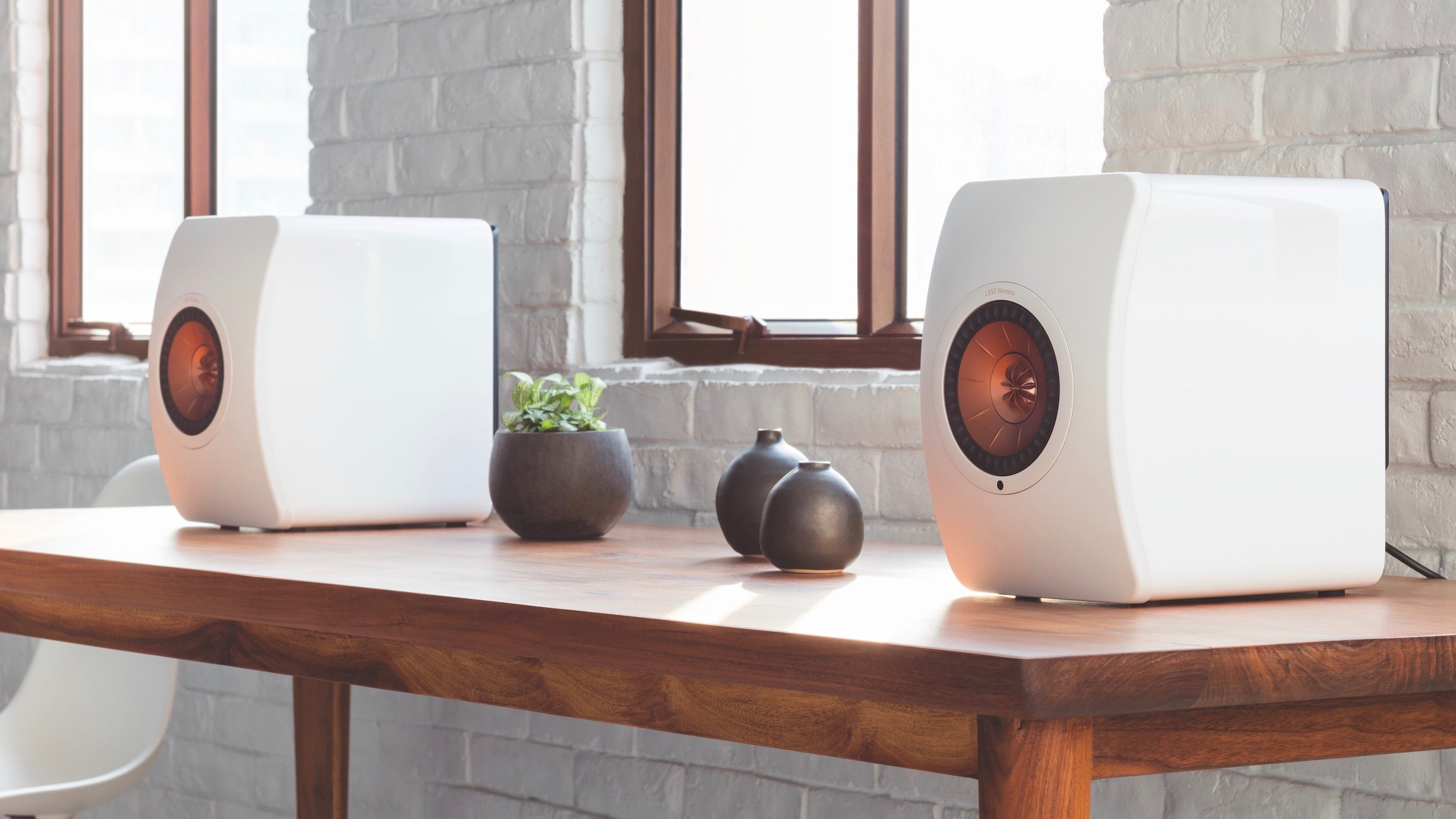 KEF LS50 Wireless speakers on a wooden table beside vases.