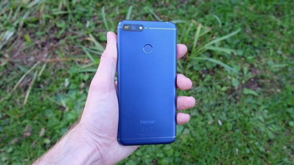 Hand holding a blue Honor 7A smartphone outdoors.