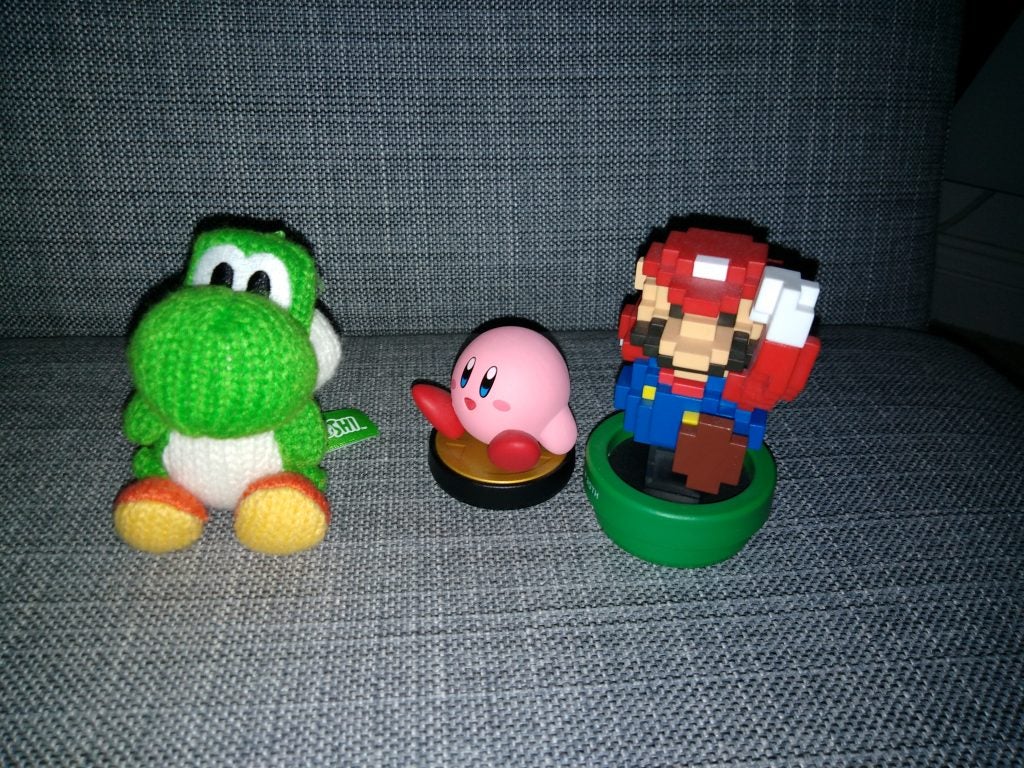 Plush Yoshi, Kirby, and Mario figurine on fabric surface.