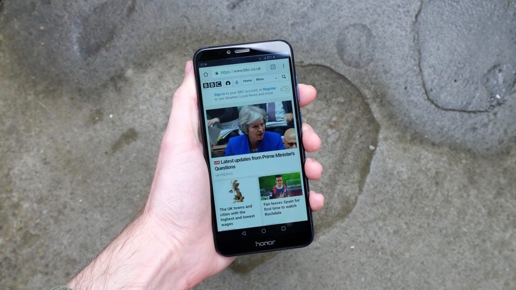 Hand holding Honor 7A smartphone displaying BBC News website.