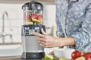 Person using Ninja Blender with fruits and vegetables inside.