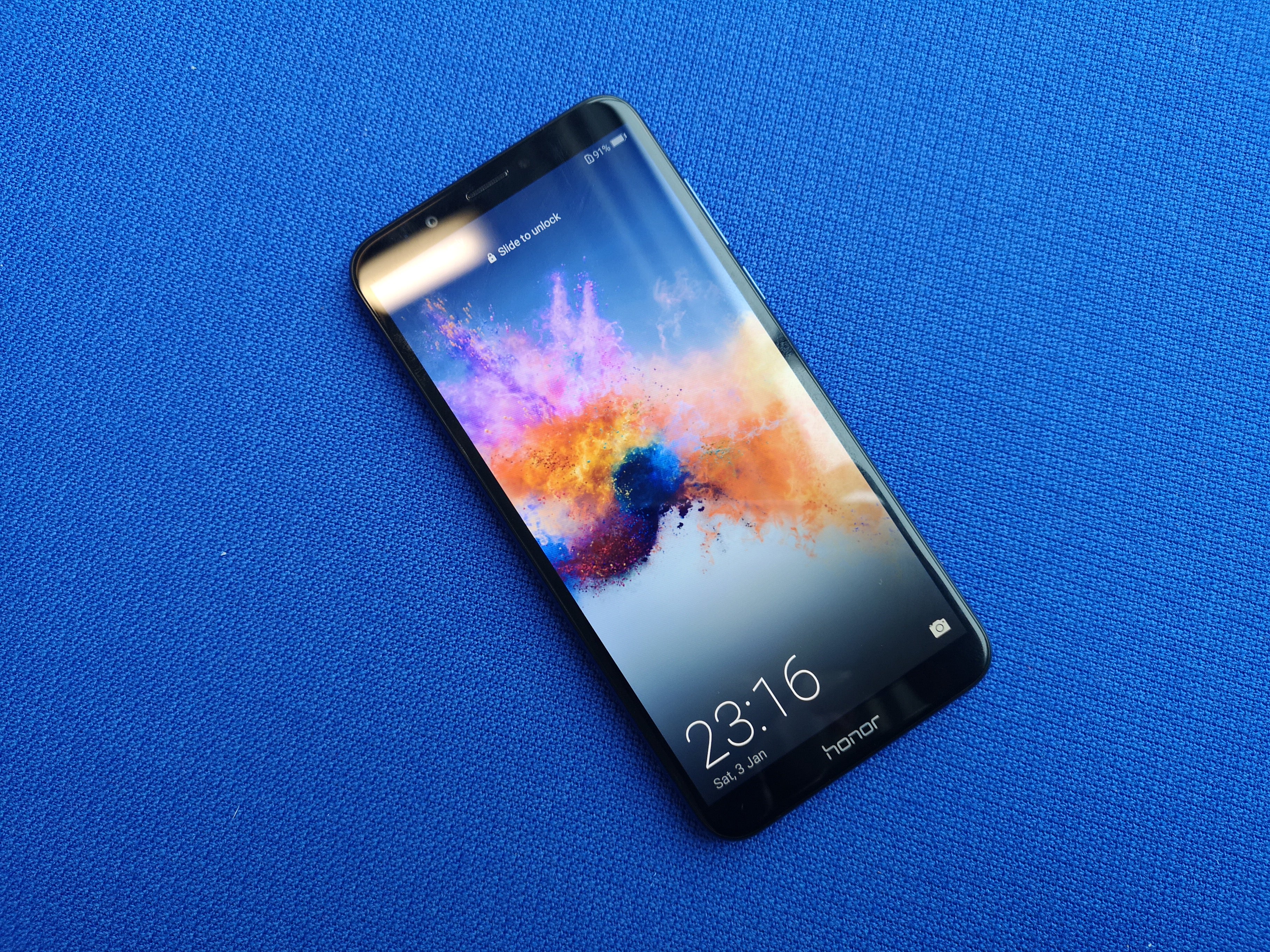 Honor 7C smartphone displaying time and colorful wallpaper.Hand holding Honor 7C smartphone with colorful wallpaper displayed.