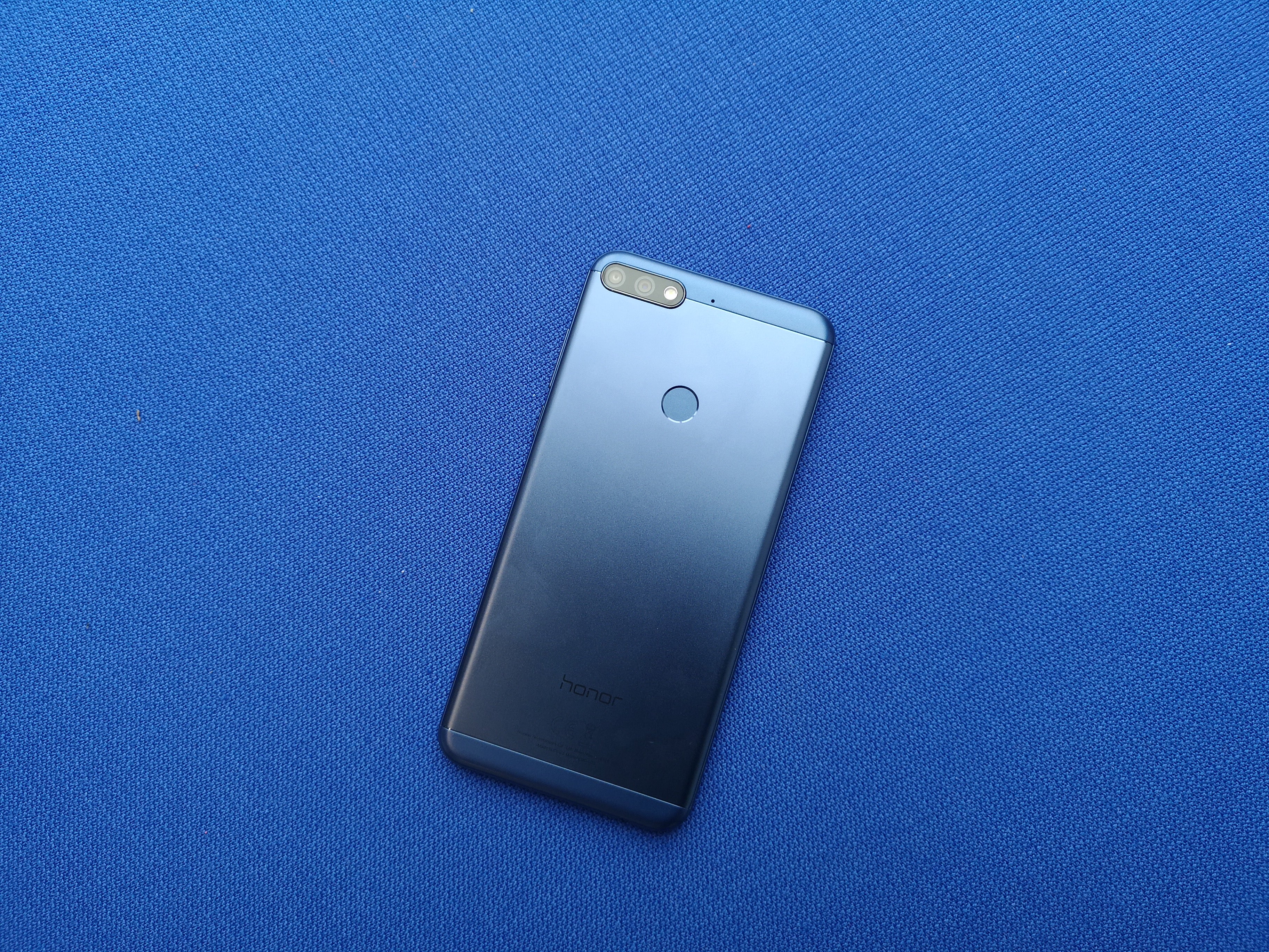 Honor 7C smartphone on blue textured background.