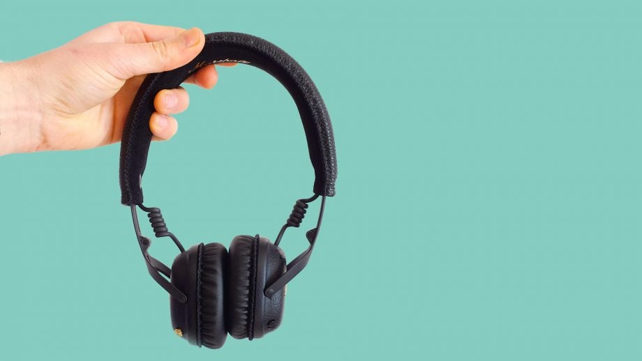 Hand holding Marshall Mid ANC headphones with teal background.