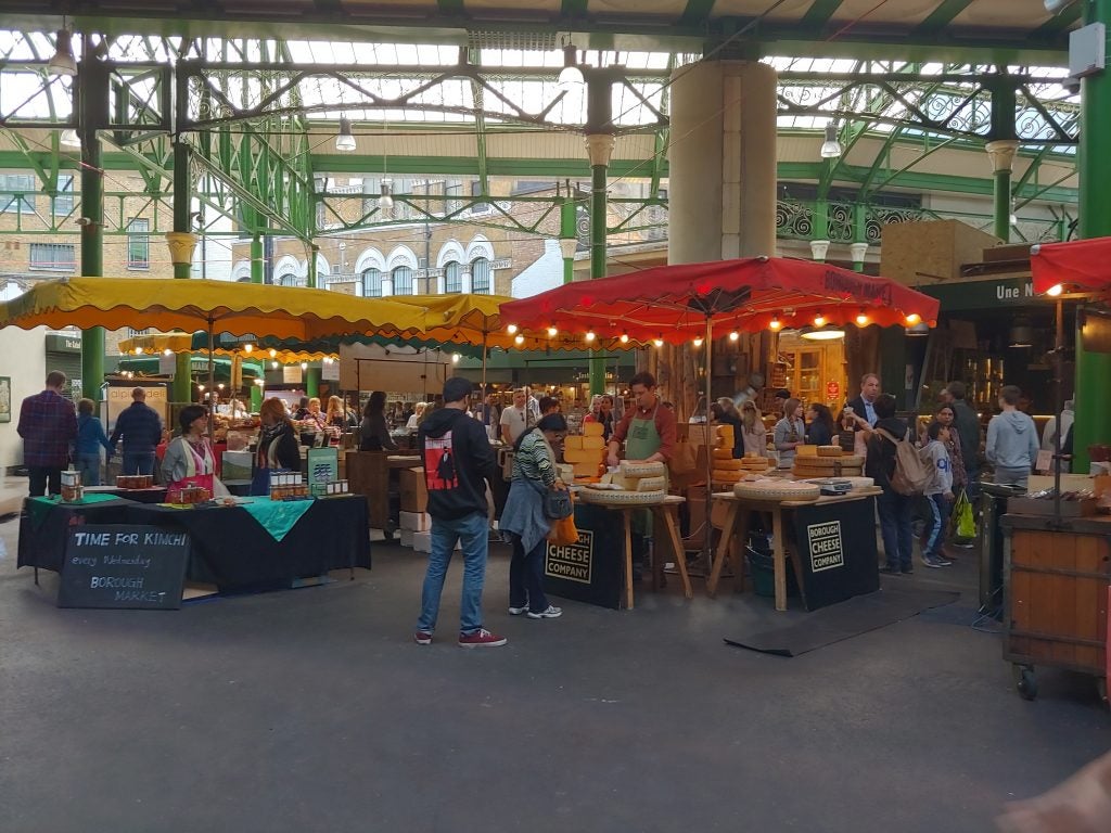 Busy indoor market scene with various food stalls and shoppers.