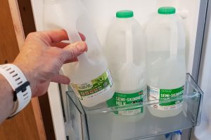 Hand reaching for milk bottles in refrigerator door shelf.
