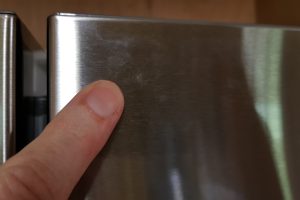 Finger pointing at a smudge on stainless steel refrigerator surface.Close-up of Bertazzoni REF90X stainless steel refrigerator door.