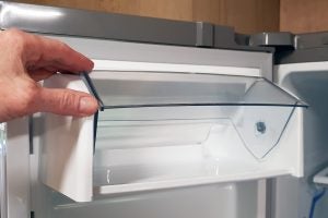 Hand opening a clear refrigerator drawer.