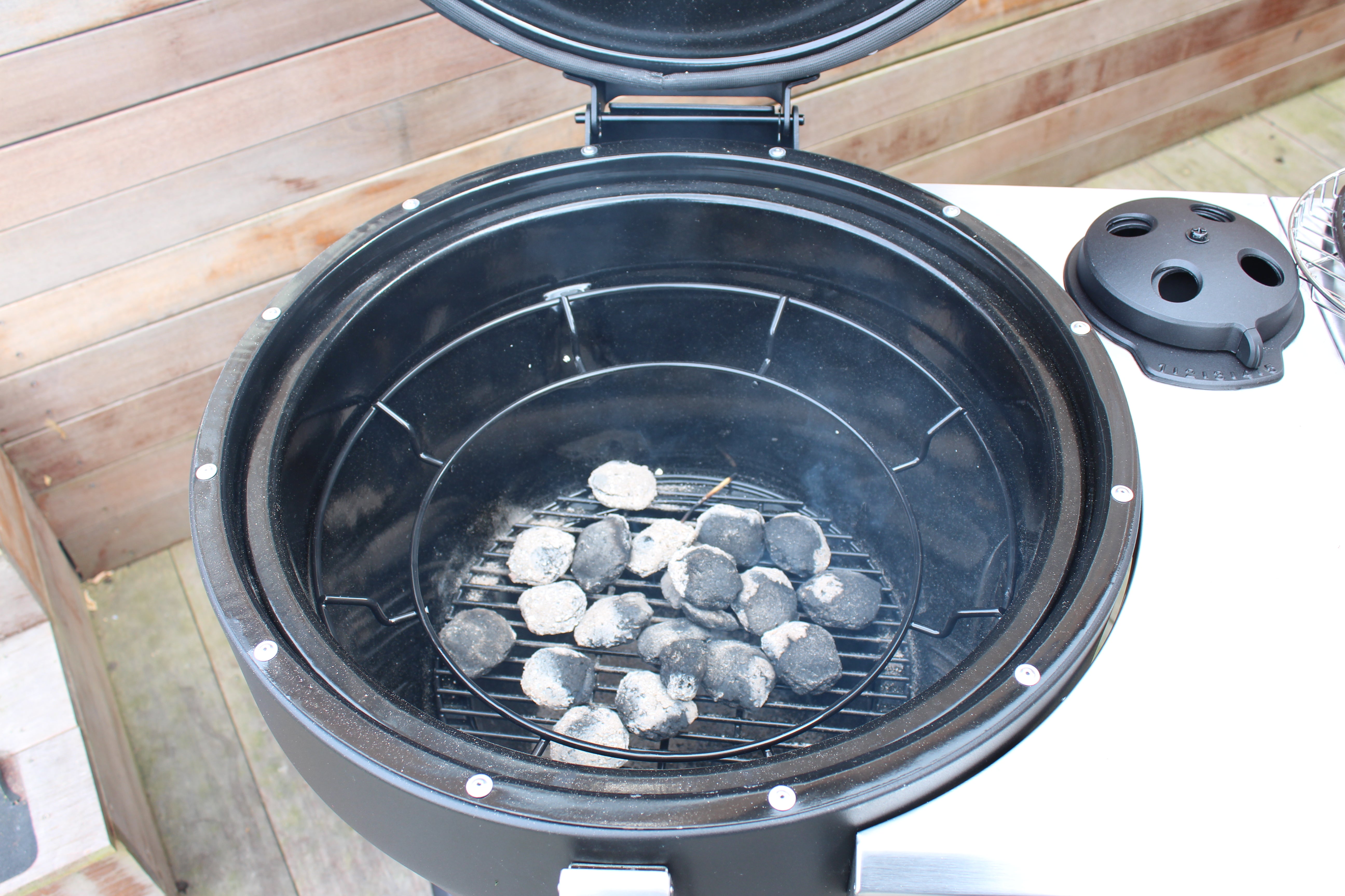 Charcoal grill interior with ash-covered coals and open lid.