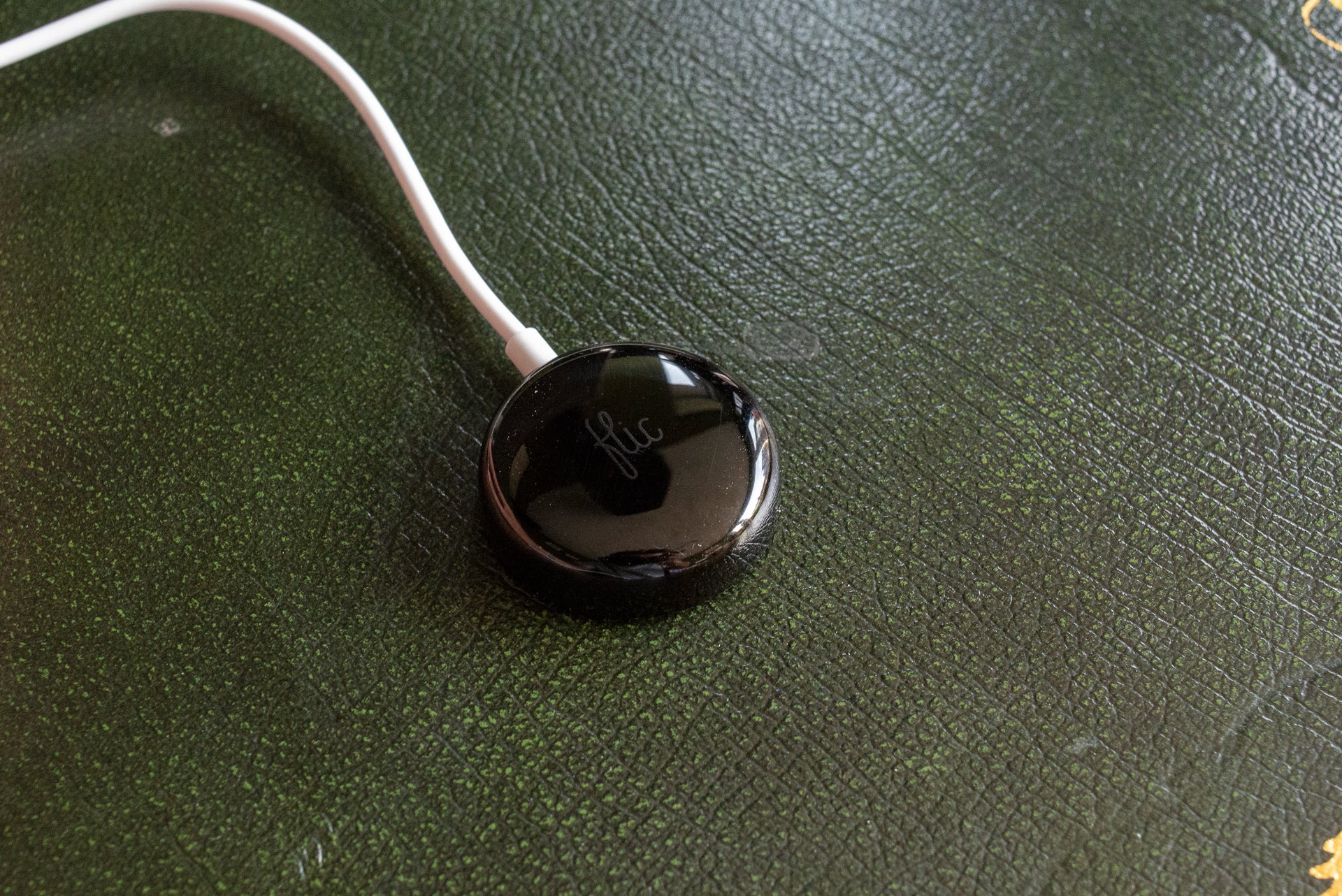 Flic smart button on textured green surface with white cable.