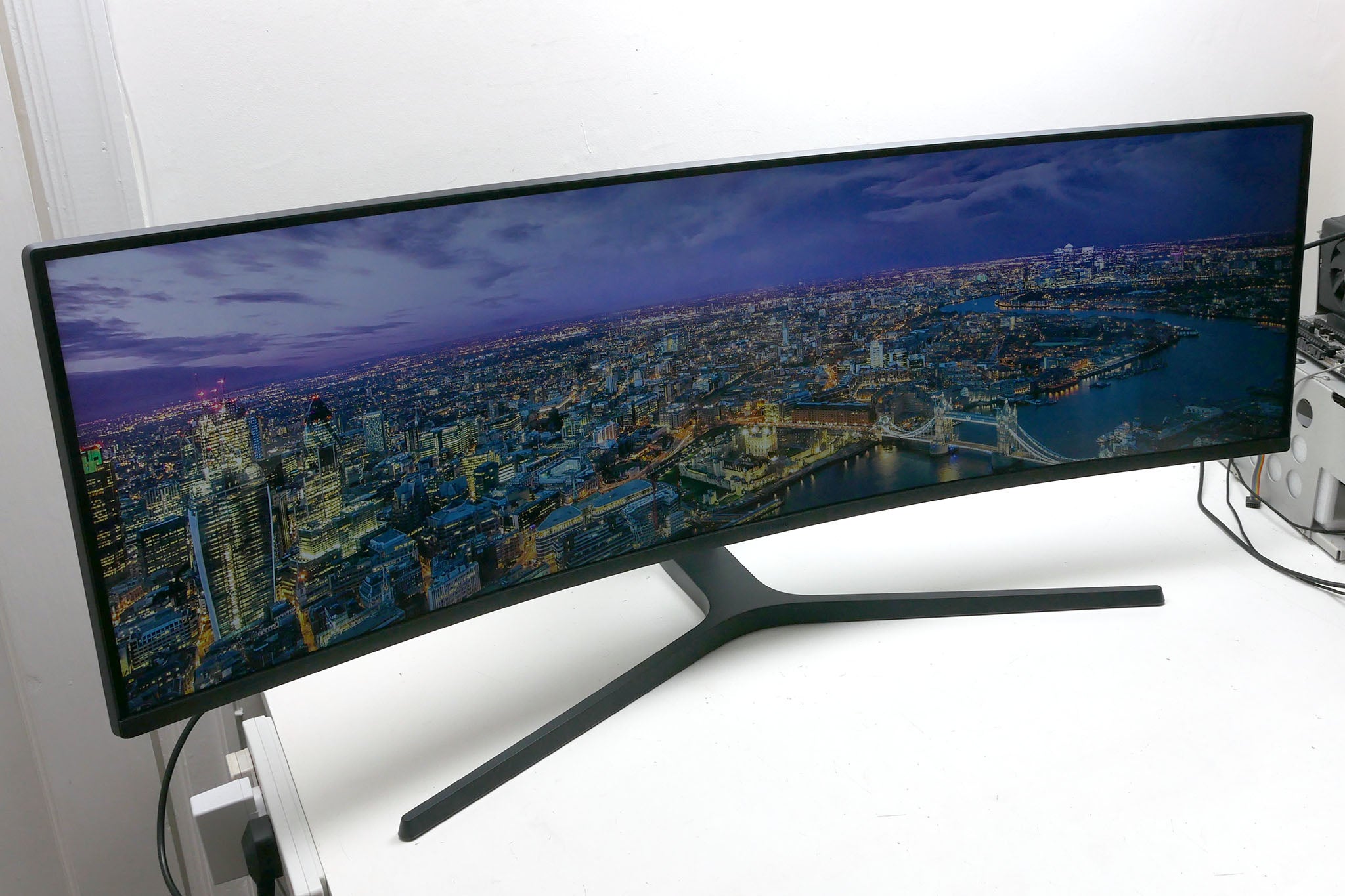 Samsung C49J89 ultra-wide monitor displaying cityscape wallpaper.