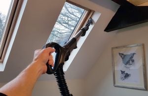 Hand using Shark Lift-Away vacuum to clean a high window.
