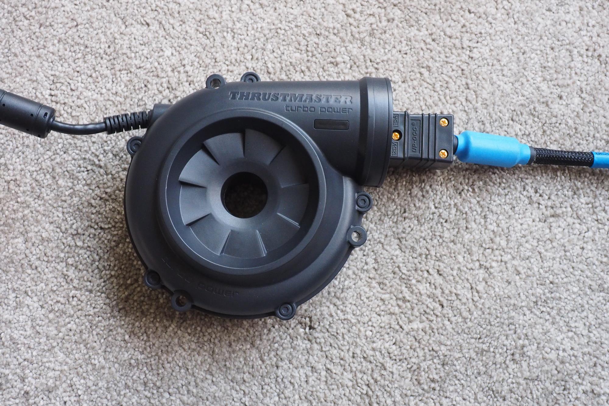 Thrustmaster T-GT racing wheel's power supply unit on carpet.