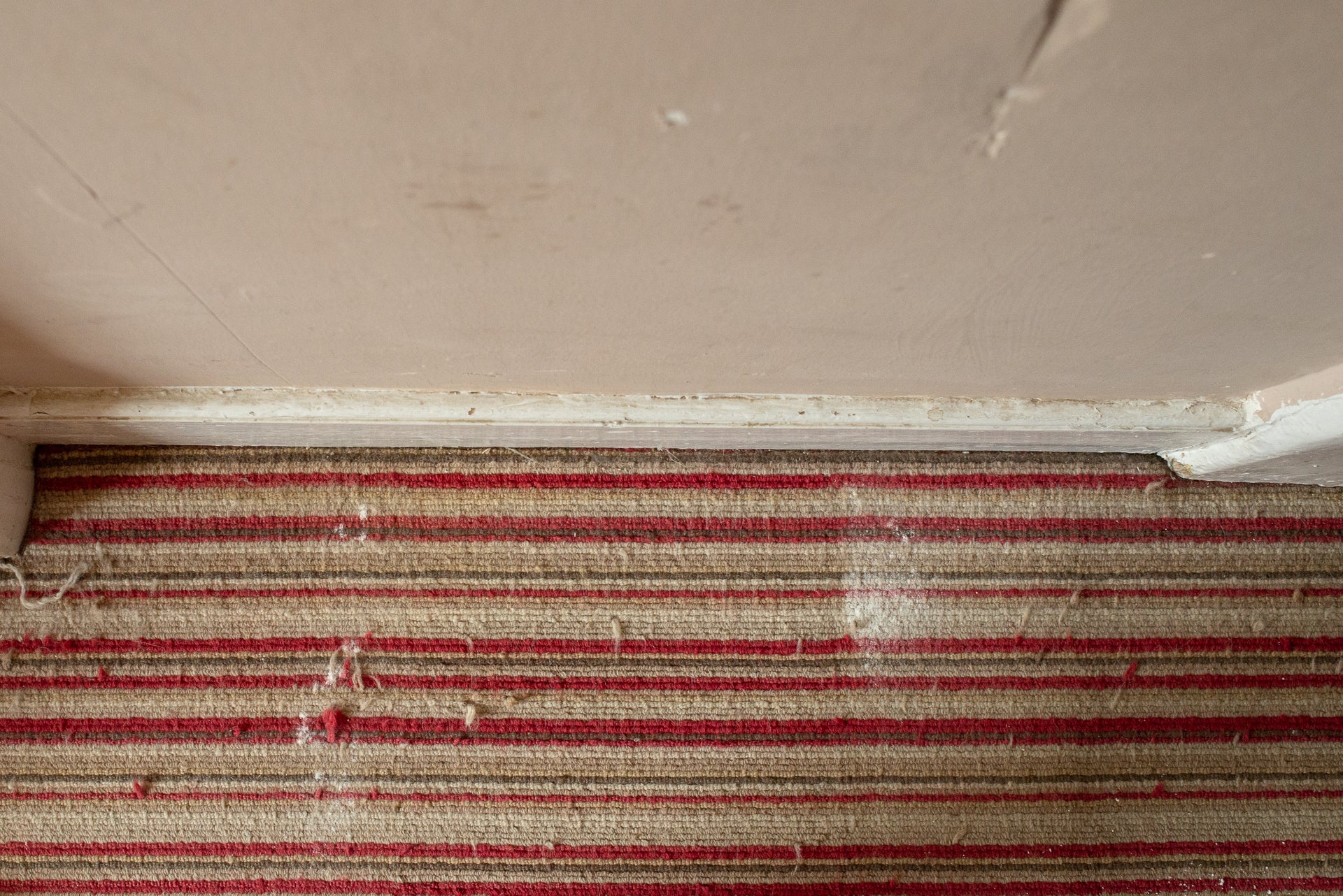 Dusty skirting board above striped carpet.