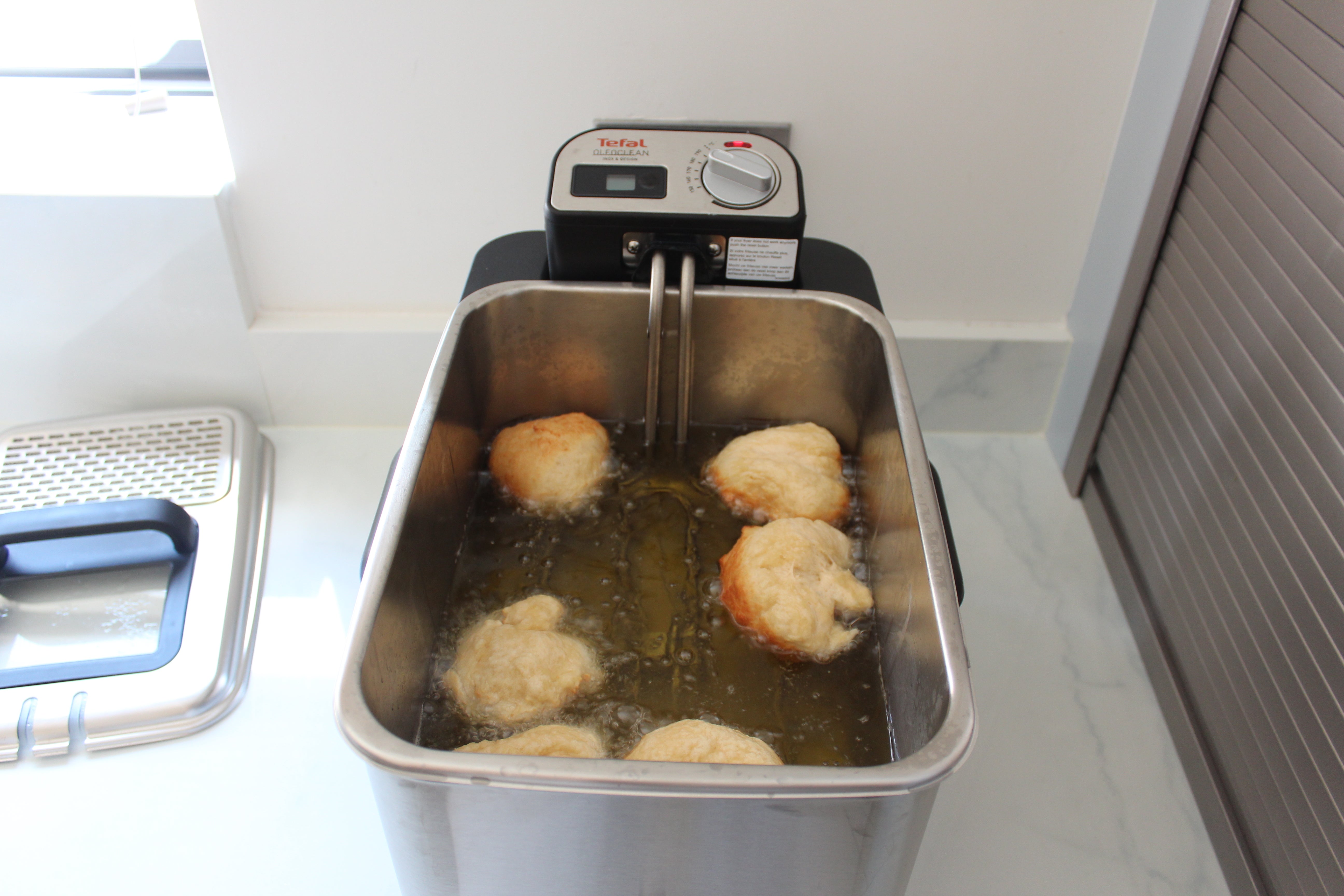 Tefal OleoClean Pro deep fryer in use with food frying.Tefal OleoClean Pro deep fryer frying chicken.Tefal FR804 OleoClean Pro deep fryer on kitchen counter.Fried treats on a plate next to Tefal OleoClean Pro fryer.
