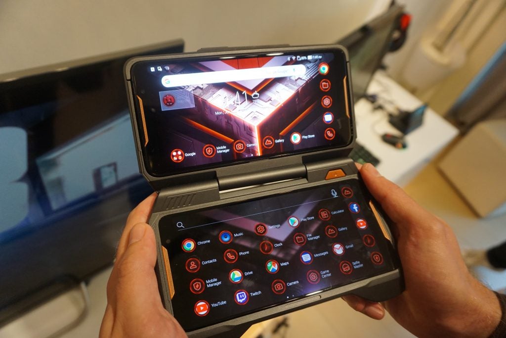 Hands holding an Asus ROG Phone with attached gaming accessory.Hand holding an Asus ROG Phone displaying apps on screen.