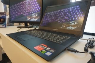 Gigabyte Sabre laptop on desk with RGB keyboard illuminated.