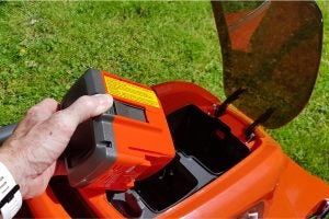 Hand inserting battery into Husqvarna LC 347VLi lawnmower.