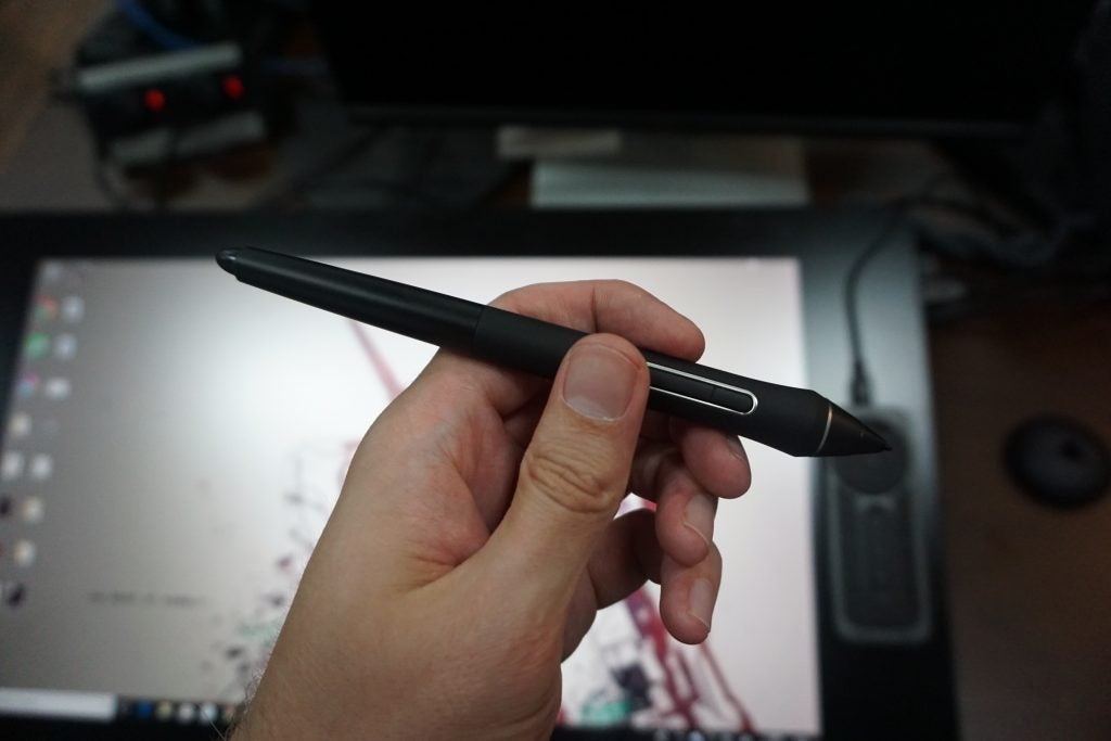 Hand holding a Wacom Cintiq Pro stylus with screen in background
