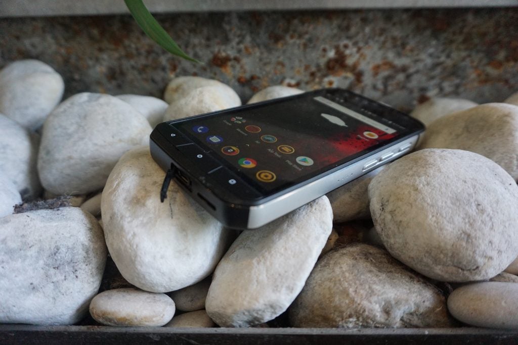 Bottom right angled view of a black Cat S61 smartphone kept on pebbles displaying homescreen