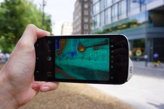 A black Cat S61 smartphone held in hand displaying a picture of street through thermal imaging camera