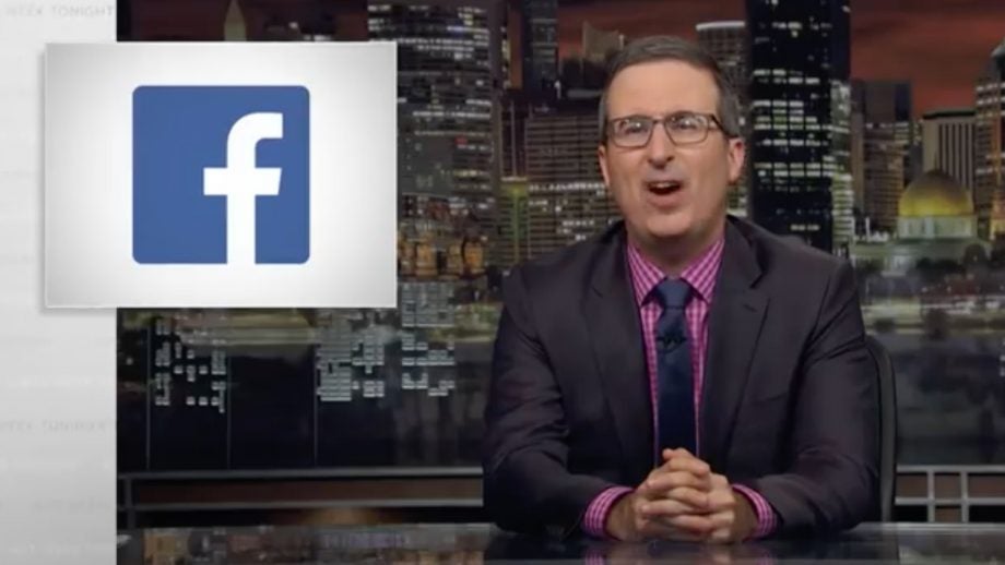 John Oliver sitting at a table with a Facebook logo beside