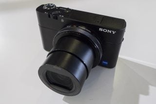 Top right angled view of a black Sony RX100 camera standing on white background