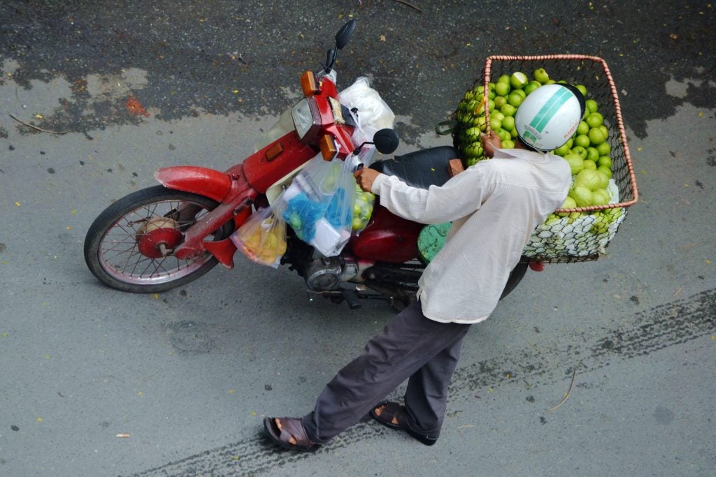 View from top of a man holding a red motorcycle with a fruit basket at it's back 