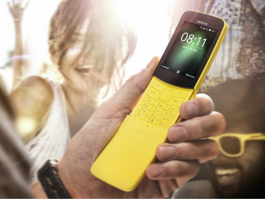 A yellow-black Nokia 8110 held in hand displaying home screen
