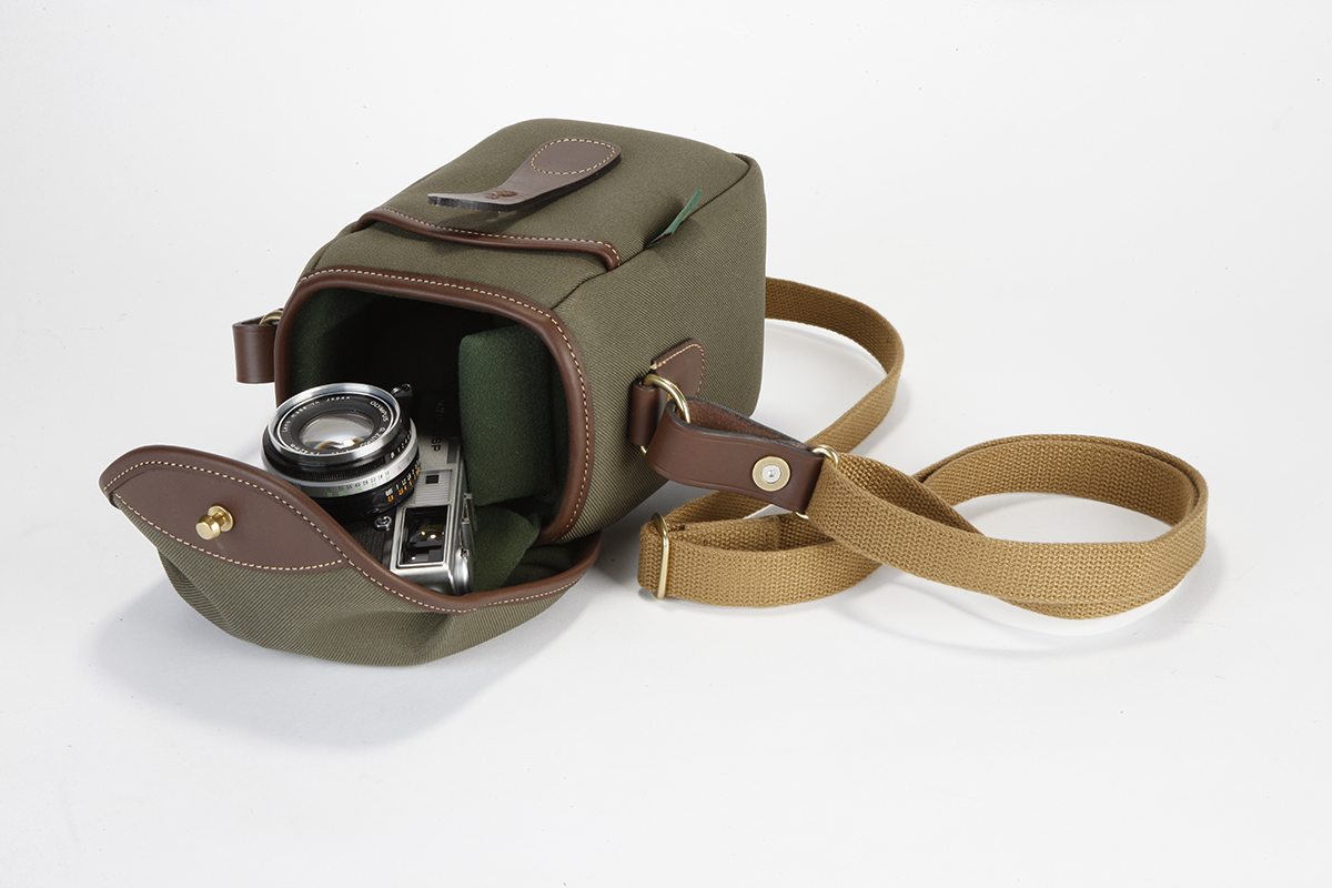 A green-brown Billingham 72 camera bag kept on a white background with a camera kept beside