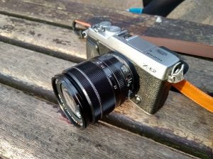 Mirrorless camera with lens on wooden bench.