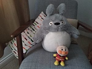 Stuffed Totoro and Anpanman toys on a chair.Scenic view of a city from a grassy hill with trees.