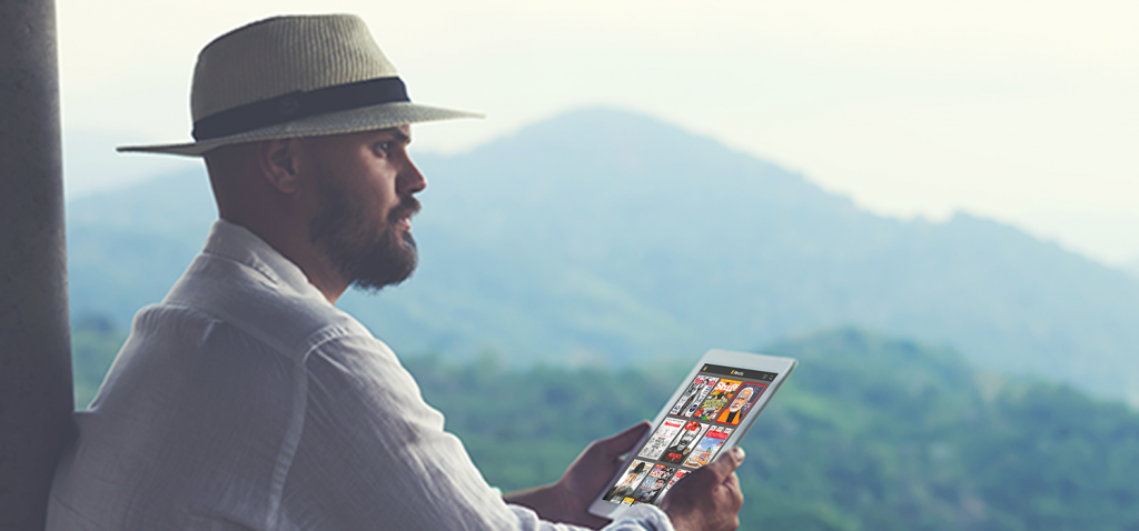 A bearded man wearing a hat sitting and holding a tablet displaying Readly's homescreen