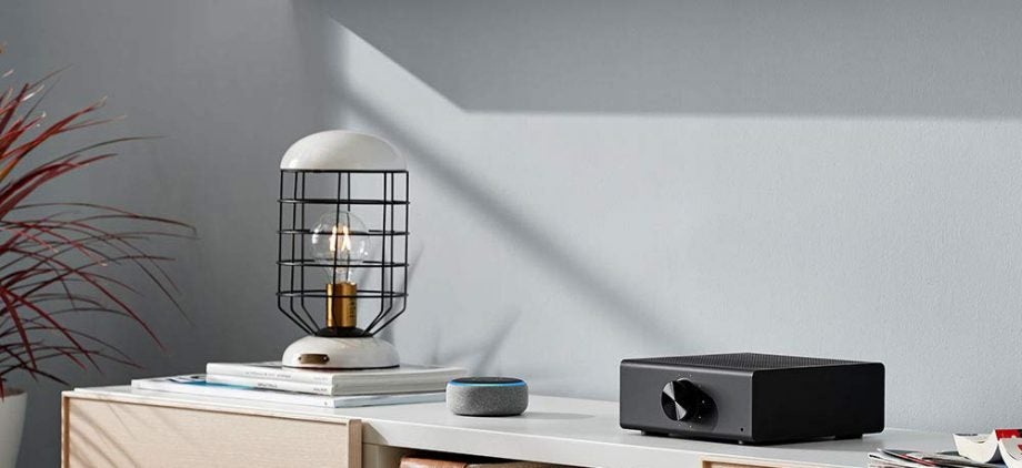 Right angled view of a black Amazon Echo Link AMP kept on a white table