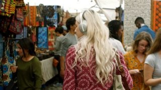 A wallpaper of Bose noise cancellation, a woman walking in a market wearing headphones