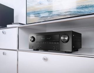 Right angled view of a black Denon AVR X2600H kept in a white shelf