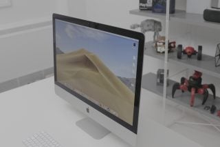 Right angled view of an iMac standing on a white table displaying homescreen