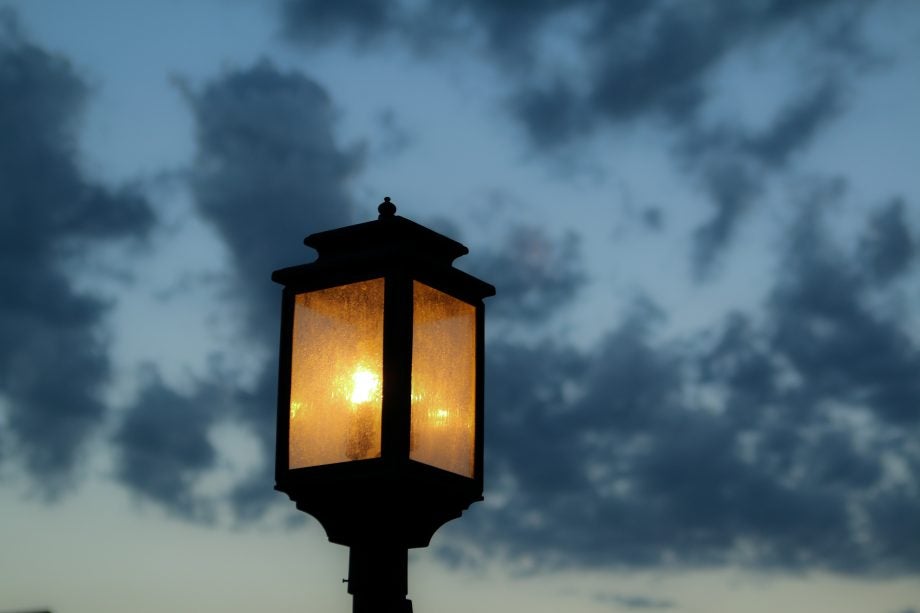 Top part view of a black lamp with orange light and blue sky behind