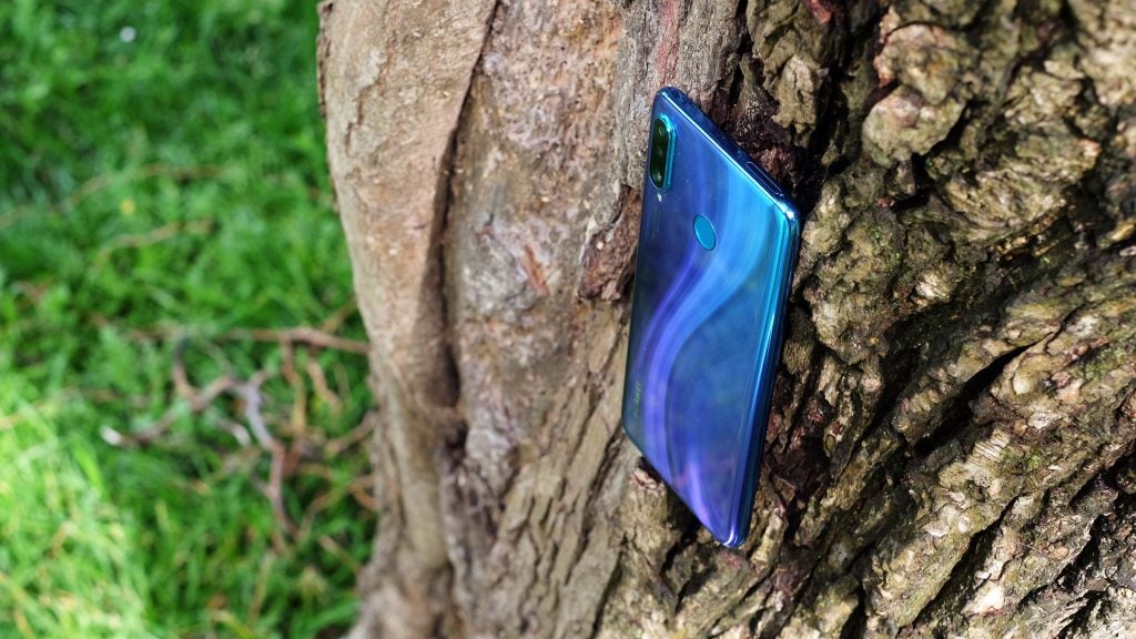 Back panel view of a blue Huawei P30 Lite standing on a tree trunk facing back
